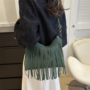 Dark green fringe crossbody bag with gold hardware shown on a model in a modern room