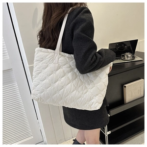 Side view of a white quilted tote bag with diamond stitching on a female model