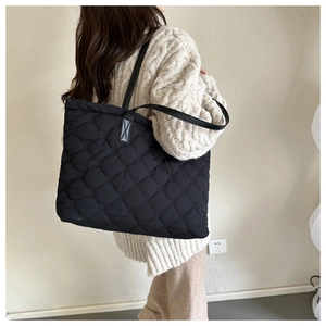 Close-up of black quilted tote bag with diamond pattern and leather strap on model