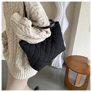 Black quilted tote bag with diamond stitching shown on shoulder in minimalist interior
