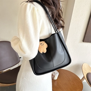 Minimalist black faux leather tote bag with yellow star pendant in a cafe setting