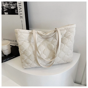 Detailed view of cream quilted puffer tote bag with rhombus pattern on a white pedestal