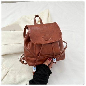 Close-up of brown faux leather mini backpack with flap, drawstring, and bead details