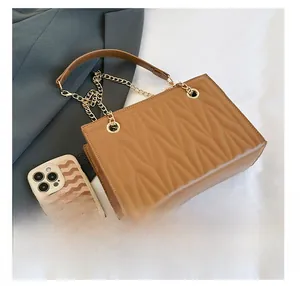 Brown quilted shoulder bag with gold chain strap shown next to a smartphone for scale