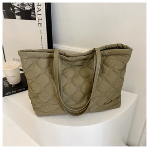 Detail of olive green quilted tote bag with intricate embroidery on a modern pedestal