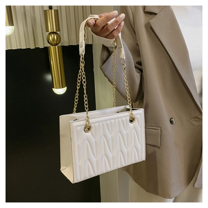 Detail of white quilted crossbody bag with golden chain strap and wavy textured pattern