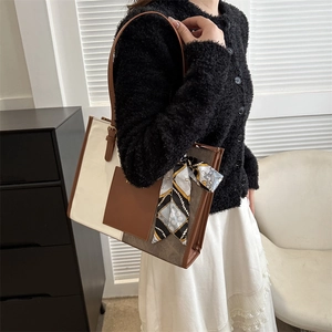 Fashionable brown and white tote bag with silk scarf on handle shown on a model