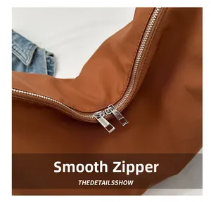 Detailed close-up of smooth silver metal double zippers on a caramel nylon shoulder bag