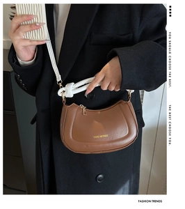 Détail du sac demi-lune en cuir marron avec bandoulière à nœud blanc et logo doré