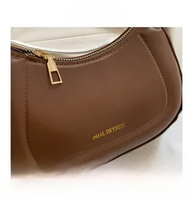 Détail du sac demi-lune en cuir marron avec fermeture éclair en métal doré et finitions