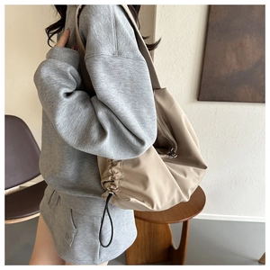 Detail of a beige pleated gym bag with silver zipper and black drawstring on a model