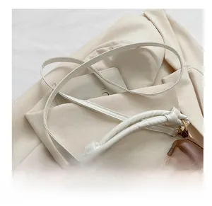 Détail d'un sac selle en cuir marron avec poignée nouée et bandoulière blanche fine