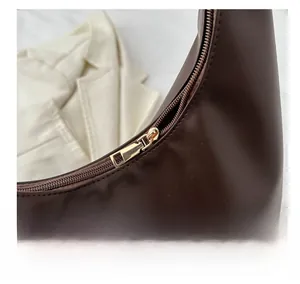 Detailed close-up of the smooth gold-tone zipper on a brown leather crescent tote bag