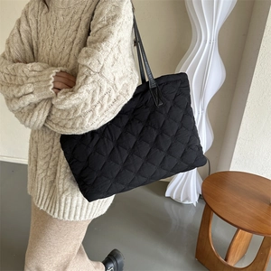 Black quilted diamond pattern tote bag with leather handles shown in a lifestyle setting