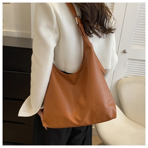 Large caramel leather tote bag with wide adjustable shoulder strap worn by a model