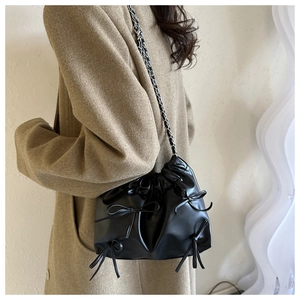 Détail d'un sac seau en cuir noir avec nœuds et bandoulière chaîne porté par un mannequin