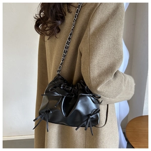 Sac bandoulière noir avec nœud et plis présenté sur un manteau en laine marron