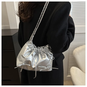 Detail of silver metallic bucket bag with leather bows and chain strap on a black coat
