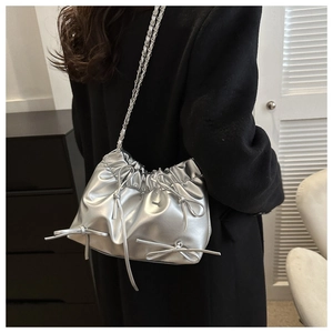 Detail of silver metallic bucket bag with leather bows and woven chain strap on shoulder