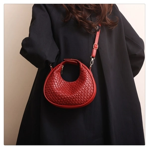 Close-up of woven dark red crescent bag on a black coat with golden hardware details