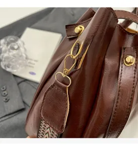 Dettaglio della ferramenta dorata e pelle marrone lucida su una borsa a secchiello