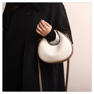 Detail showing cream woven crescent bag with brown leather trim and gold hardware