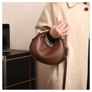 Detail of woven texture on a dark brown crescent hobo bag paired with a trench coat