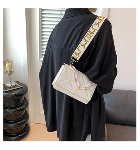 White quilted square bag with gold chain and abstract patterned wide strap on a model