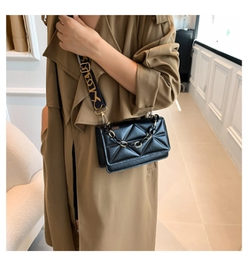 Detail of black quilted crossbody bag with chunky chain and wide printed strap