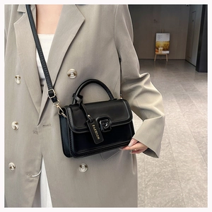 Detail of a black PU leather crossbody bag with metal buckle on a grey oversized suit