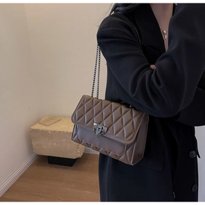 Detailed view of coffee brown quilted chain bag with elegant metal buckle on a dark blazer