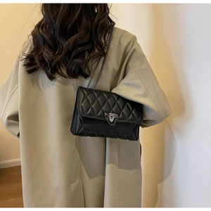Close-up of black quilted crossbody bag with metal chain strap and luxury buckle
