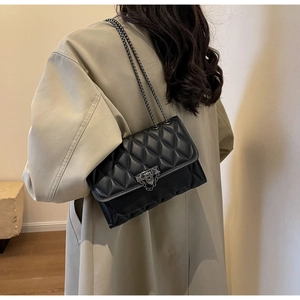 Detail of a black quilted crossbody bag with silver chain strap on a trench coat