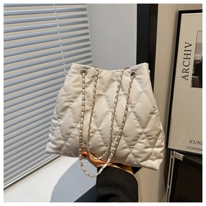 Detailed shot of cream quilted tote bag with gold chain strap on minimalist background