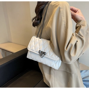 Detail of white quilted chain bag featuring a gray metal lock and shoulder strap