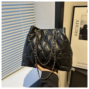 Detail of black quilted tote bag featuring golden chain strap and leather texture