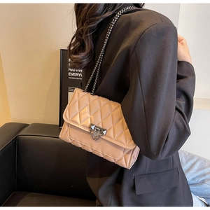 Detail of light beige quilted crossbody bag with gunmetal chain and turn-lock closure