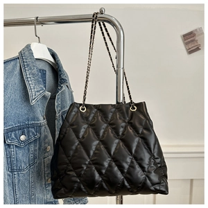Detail of black quilted tote bag with golden chain strap hanging on a metal hanger
