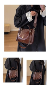 Dettaglio della borsa tote marrone scuro con tracolla intrecciata e logo dorato