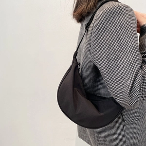 Minimalist black nylon crescent crossbody bag shown on model with houndstooth jacket