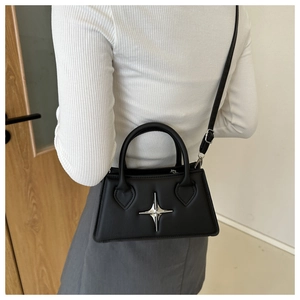 Detail of a black trapezoid crossbody bag featuring a silver star buckle on a model