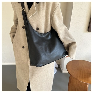 Detail of black textured PU leather tote bag worn with a chic beige wool coat