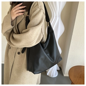 Close-up of a black pebbled leather Hobo bag with gold hardware worn on an oatmeal coat