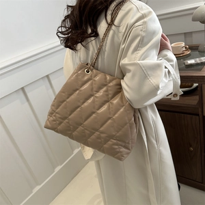Minimalist beige quilted tote bag with metal chain strap shown in an elegant setting