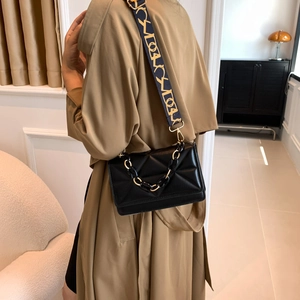 Quilted black flap handbag with patterned shoulder strap on trench coat model