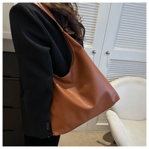 Side view of large brown lychee grain PU leather hobo bag worn by model in home setting