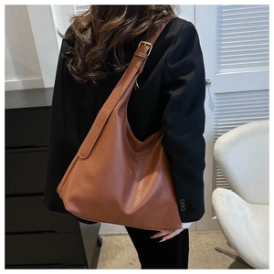 Detail of deep caramel brown tote bag showing pebbled leather texture and metal buckles