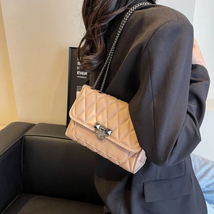 Quilted apricot crossbody bag with a metal lock and chain strap on a model