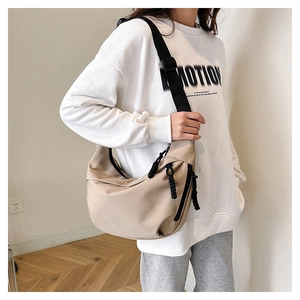 Detail of adjustable black shoulder strap and woven zipper on beige nylon dumpling bag