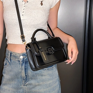 Women's black matte crossbody bag with metal lock and round handle shown on model